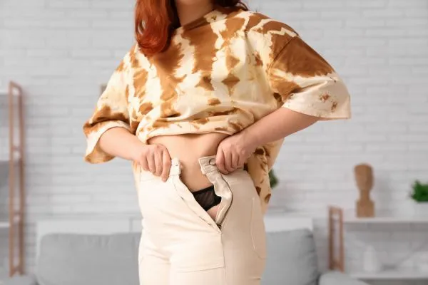 Image of woman trying to do her trousers up after pregnancy weight gain Finchampstead